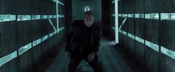 Movie still from “Resident Evil: The Final Chapter” (2016), directed by Paul W.S. Anderson – A man in a suit and tie standing in a dark hallway; Medium shot, Low angle