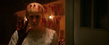 Movie still from “Resident Evil: Welcome to Raccoon City” (2021), directed by Johannes Roberts – A woman with blood on her face looking out of a window; Close Up shot, Low angle