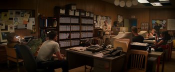 Movie still from “Resident Evil: Welcome to Raccoon City” (2021), directed by Johannes Roberts – A man standing in front of a desk in a room; Wide shot, Over the shoulder angle