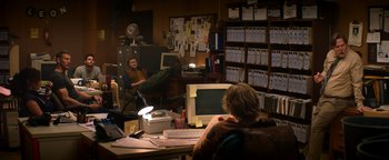 Movie still from “Resident Evil: Welcome to Raccoon City” (2021), directed by Johannes Roberts – Two people sitting in front of computers in an office; Wide shot, Over the shoulder angle