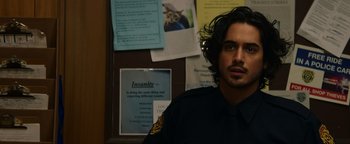 Movie still from “Resident Evil: Welcome to Raccoon City” (2021), directed by Johannes Roberts – A man in a police uniform standing in front of a bulletin board; Close Up shot, Over the shoulder angle