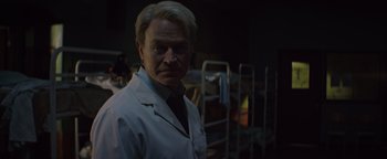 Movie still from “Resident Evil: Welcome to Raccoon City” (2021), directed by Johannes Roberts – A man wearing a lab coat standing in a room; Medium shot, Over the shoulder angle