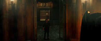 Movie still from “Resident Evil: Welcome to Raccoon City” (2021), directed by Johannes Roberts – A man standing in a dark room with a sign above him; Wide shot, High angle