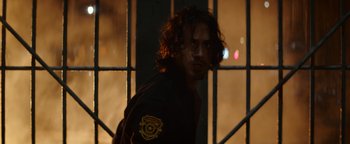Movie still from “Resident Evil: Welcome to Raccoon City” (2021), directed by Johannes Roberts – A man with long curly hair wearing a police uniform; Close Up shot, Over the shoulder angle