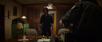 Movie still from “Resident Evil: Welcome to Raccoon City” (2021), directed by Johannes Roberts – A man standing in front of a table in a room; Medium shot, Over the shoulder angle