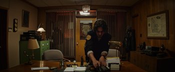 Movie still from “Resident Evil: Welcome to Raccoon City” (2021), directed by Johannes Roberts – A man in black shirt at a table with a calculator; Medium shot, Low angle