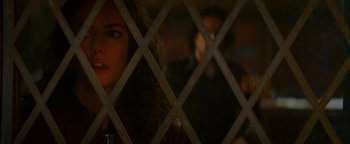 Movie still from “Resident Evil: Welcome to Raccoon City” (2021), directed by Johannes Roberts – A woman looking through a lattice in a room; Close Up shot, Over the shoulder angle