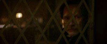 Movie still from “Resident Evil: Welcome to Raccoon City” (2021), directed by Johannes Roberts – A man looking through a lattice in a room; Close Up shot, Over the shoulder angle