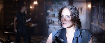 Movie still from “Resident Evil: Welcome to Raccoon City” (2021), directed by Johannes Roberts – A woman with curly hair and a microphone; Close Up shot, High angle