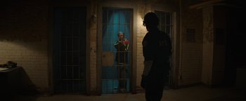 Movie still from “Resident Evil: Welcome to Raccoon City” (2021), directed by Johannes Roberts – A man standing next to a door in a room; Wide shot, Over the shoulder angle