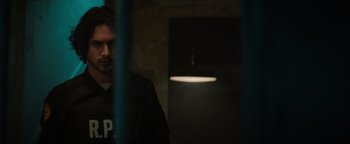 Movie still from “Resident Evil: Welcome to Raccoon City” (2021), directed by Johannes Roberts – A man standing next to a light in a room; Medium shot, Over the shoulder angle