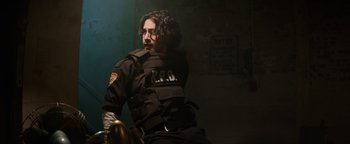 Movie still from “Resident Evil: Welcome to Raccoon City” (2021), directed by Johannes Roberts – A man in a police uniform sitting in a chair; Medium shot, Low angle