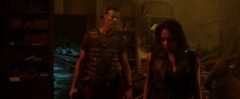 Movie still from “Resident Evil: Welcome to Raccoon City” (2021), directed by Johannes Roberts – A man and a woman are standing in a dark room; Medium shot, Over the shoulder angle