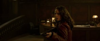 Movie still from “Resident Evil: Welcome to Raccoon City” (2021), directed by Johannes Roberts – A woman holding a gun while standing in a dark room; Medium shot, Over the shoulder angle