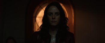 Movie still from “Resident Evil: Welcome to Raccoon City” (2021), directed by Johannes Roberts – A woman with long dark hair is standing in front of an arched window; Close Up shot, Low angle