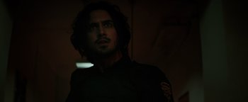 Movie still from “Resident Evil: Welcome to Raccoon City” (2021), directed by Johannes Roberts – A man with long black hair is looking at the camera; Close Up shot, Over the shoulder angle