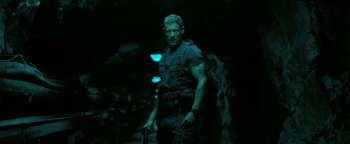 Movie still from “Resident Evil: Welcome to Raccoon City” (2021), directed by Johannes Roberts – A man holding a gun while standing in a dark cave; Medium shot, Low angle