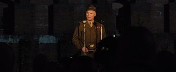 Movie still from “Resistance” (2020), directed by Jonathan Jakubowicz – A man in a military uniform is holding a microphone; Medium shot, Low angle