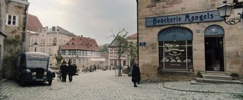 Movie still from “Resistance” (2020), directed by Jonathan Jakubowicz – A woman walking down a street past a building; Extreme Wide shot, High angle