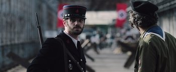 Movie still from “Resistance” (2020), directed by Jonathan Jakubowicz – A man in a uniform is standing in front of flags; Medium shot, Over the shoulder angle
