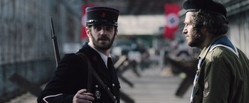 Movie still from “Resistance” (2020), directed by Jonathan Jakubowicz – A man in a uniform is standing outside; Medium shot, Low angle