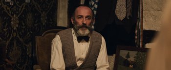 Movie still from “Resistance” (2020), directed by Jonathan Jakubowicz – An older man with a beard and a bow tie; Medium shot, Low angle