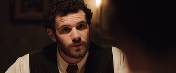 Movie still from “Resistance” (2020), directed by Jonathan Jakubowicz – A person with curly hair and a beard; Close Up shot, Over the shoulder angle