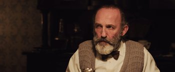 Movie still from “Resistance” (2020), directed by Jonathan Jakubowicz – An older man with a beard and a bow tie; Close Up shot, Over the shoulder angle