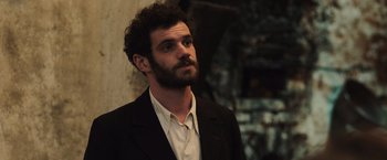 Movie still from “Resistance” (2020), directed by Jonathan Jakubowicz – A man with a beard wearing a suit; Close Up shot, Over the shoulder angle