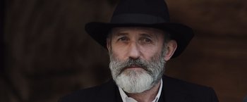 Movie still from “Resistance” (2020), directed by Jonathan Jakubowicz – An older man with a beard wearing a black hat; Close Up shot, Low angle