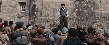 Movie still from “Resistance” (2020), directed by Jonathan Jakubowicz – A man standing in front of a group of people; Wide shot, Low angle