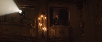 Movie still from “Resistance” (2020), directed by Jonathan Jakubowicz – A man standing on a window ledge in front of a wall of lit candles; Wide shot, Low angle