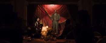 Movie still from “Resistance” (2020), directed by Jonathan Jakubowicz – A man standing in front of a stage with candles in front of him; Wide shot, Low angle