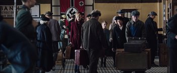 Movie still from “Resistance” (2020), directed by Jonathan Jakubowicz – A group of people with suitcases walking down a hall way; Wide shot, High angle