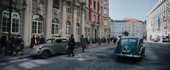 Movie still from “Resistance” (2020), directed by Jonathan Jakubowicz – A group of people walking down a street near a building; Wide shot, High angle