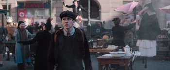 Movie still from “Resistance” (2020), directed by Jonathan Jakubowicz – A man in a hat and a jacket walking down a street; Medium shot, High angle