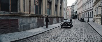 Movie still from “Resistance” (2020), directed by Jonathan Jakubowicz – An old car parked on the side of the street; Wide shot, High angle