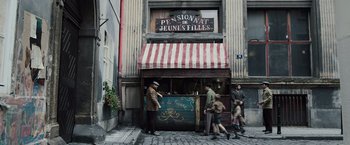 Movie still from “Resistance” (2020), directed by Jonathan Jakubowicz – A group of people walking on a sidewalk near a building; Wide shot, High angle