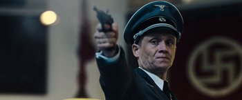 Movie still from “Resistance” (2020), directed by Jonathan Jakubowicz – A man in a uniform holding a gun up in the air; Close Up shot, Low angle
