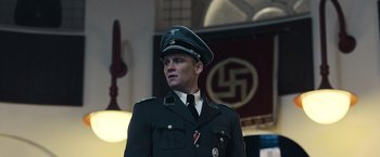 Movie still from “Resistance” (2020), directed by Jonathan Jakubowicz – A man in a military uniform stands in front of a swastika; Medium shot, Low angle