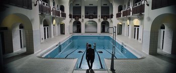 Movie still from “Resistance” (2020), directed by Jonathan Jakubowicz – A man standing in front of an indoor swimming pool; Extreme Wide shot, High angle