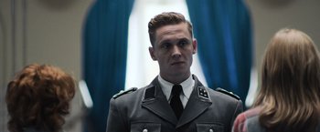 Movie still from “Resistance” (2020), directed by Jonathan Jakubowicz – A man in a military uniform stands in front of a blue curtain; Close Up shot, Low angle