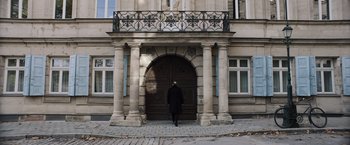 Movie still from “Resistance” (2020), directed by Jonathan Jakubowicz – A person standing in front of an entrance to a building; Wide shot, Low angle