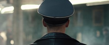 Movie still from “Resistance” (2020), directed by Jonathan Jakubowicz – A man wearing a black leather jacket and a hat; Close Up shot, Over the shoulder angle