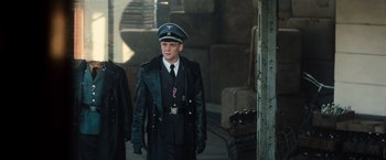 Movie still from “Resistance” (2020), directed by Jonathan Jakubowicz – A man in a leather jacket wearing a hat; Medium shot, Low angle