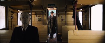 Movie still from “Resistance” (2020), directed by Jonathan Jakubowicz – A man in a suit and tie standing in a train car; Wide shot, Low angle