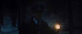 Movie still from “Resistance” (2020), directed by Jonathan Jakubowicz – A man in a military uniform is standing in the dark with a flashlight; Medium shot, Over the shoulder angle