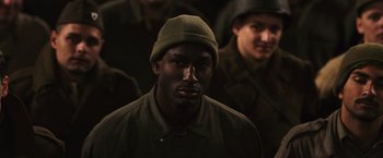 Movie still from “Resistance” (2020), directed by Jonathan Jakubowicz – A man wearing a green hat in front of a group of soldiers; Close Up shot, High angle