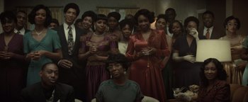 Movie still from “Respect” (2021), directed by Liesl Tommy – A group of people standing in a room; Medium shot, High angle