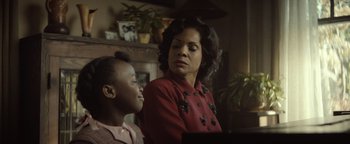 Movie still from “Respect” (2021), directed by Liesl Tommy – A woman and a boy in a living room next to a fireplace; Medium shot, Over the shoulder angle
